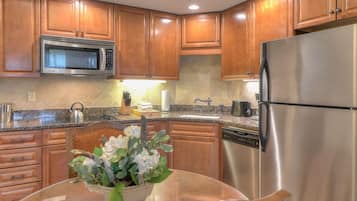 A modern kitchen with wooden cabinets, stainless steel appliances, granite countertops, and a glass dining table with a floral centerpiece.
