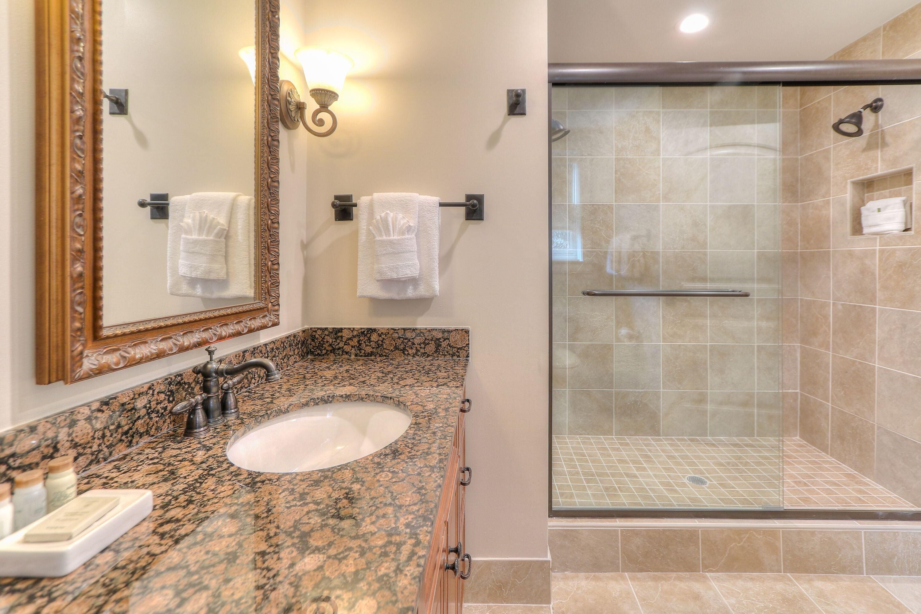 A bathroom with a granite countertop sink, a large mirror, and a glass-enclosed shower area.
