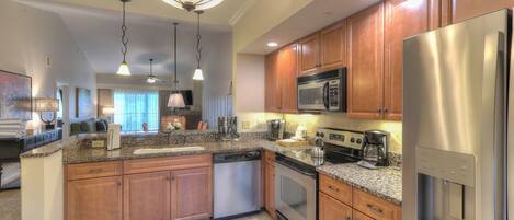 A modern kitchen with granite countertops, stainless steel appliances, wooden cabinets, and pendant lighting.