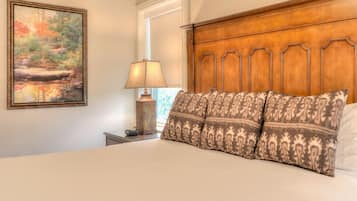 A neatly made bed with patterned pillows, a wooden headboard, a bedside lamp, and a framed painting on the wall.