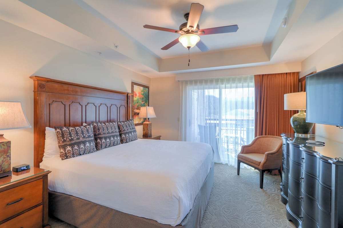 A hotel room with a large bed, a ceiling fan, a chair, a dresser, and a window with curtains.