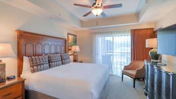 Una habitación de hotel con una cama grande, un ventilador de techo, una silla, un aparador y una ventana con cortinas.