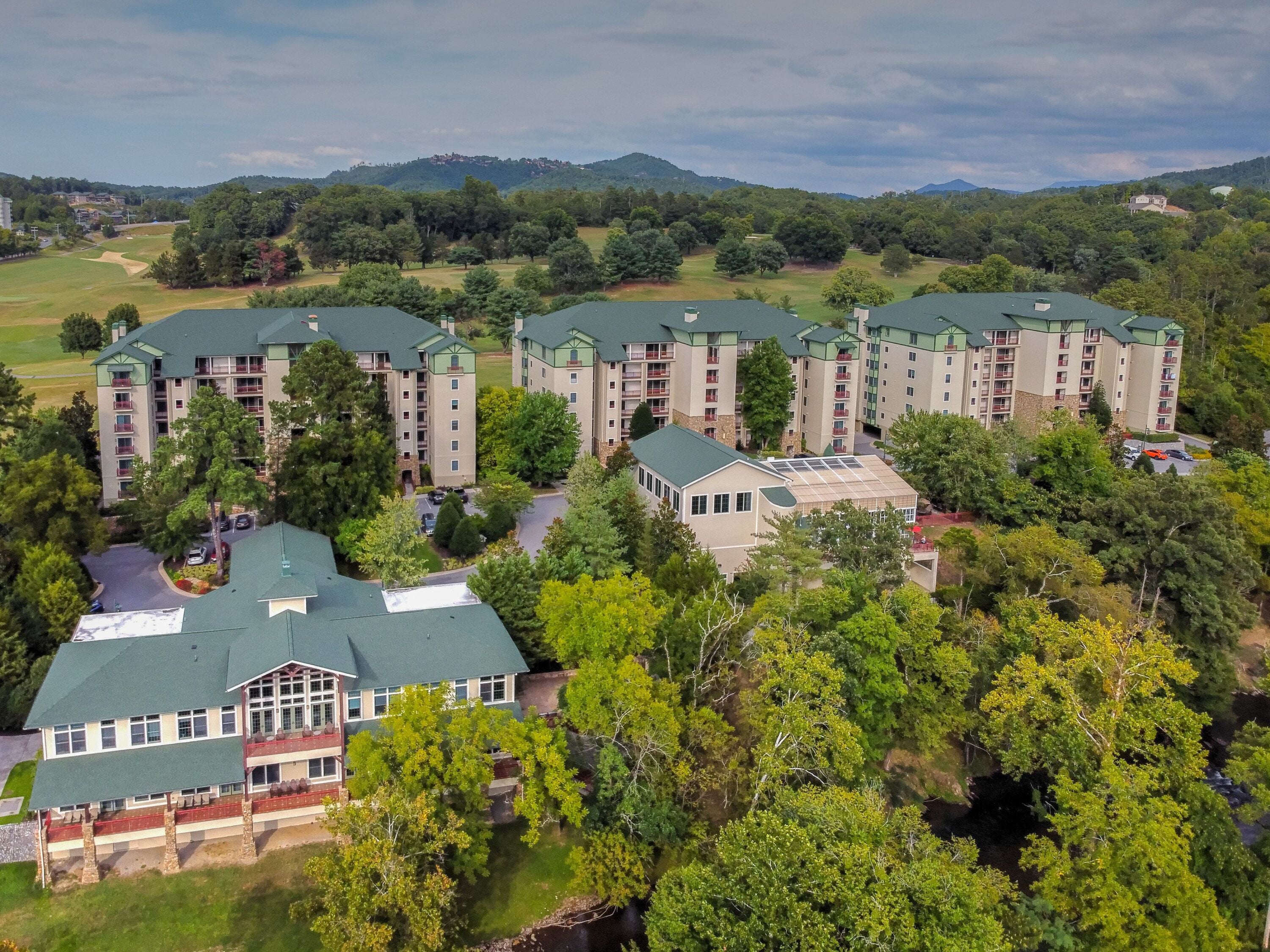 Un hotel de varios pisos con techo verde, rodeado de exuberante vegetación y un campo de golf al fondo.