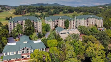 Un hotel de varios pisos con techo verde, rodeado de exuberante vegetación y un campo de golf al fondo.