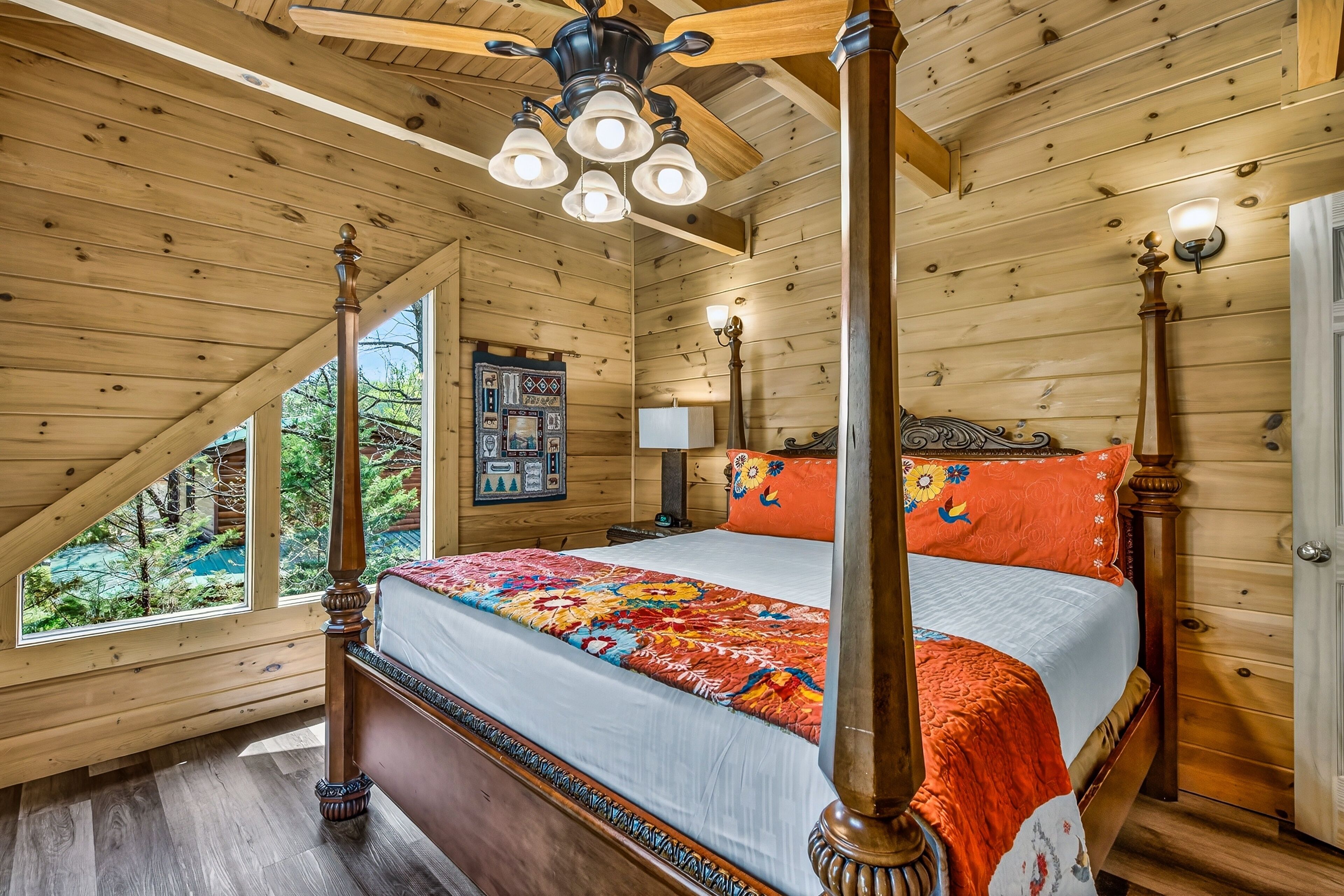 Ein Himmelsbett mit farbenfroher Quilttdecke, Holzbalkendecke und einem Fenster mit Blick auf Grünflächen.