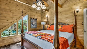 A four-poster bed with a colorful quilt, wooden ceiling beams, and a window with a view of greenery.