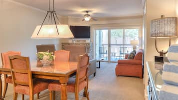A dining area with a wooden table and chairs, a ceiling fan, and a large window with a view of the outdoors.