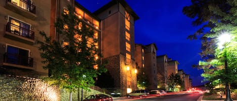 Un immeuble à plusieurs étages, doté de balcons et d’une façade en pierre, entouré d’arbres et bordé d’une rue bien éclairée.