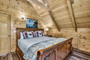 A wooden bedroom with a bed, a nightstand, a wall-mounted lamp, and a painting.