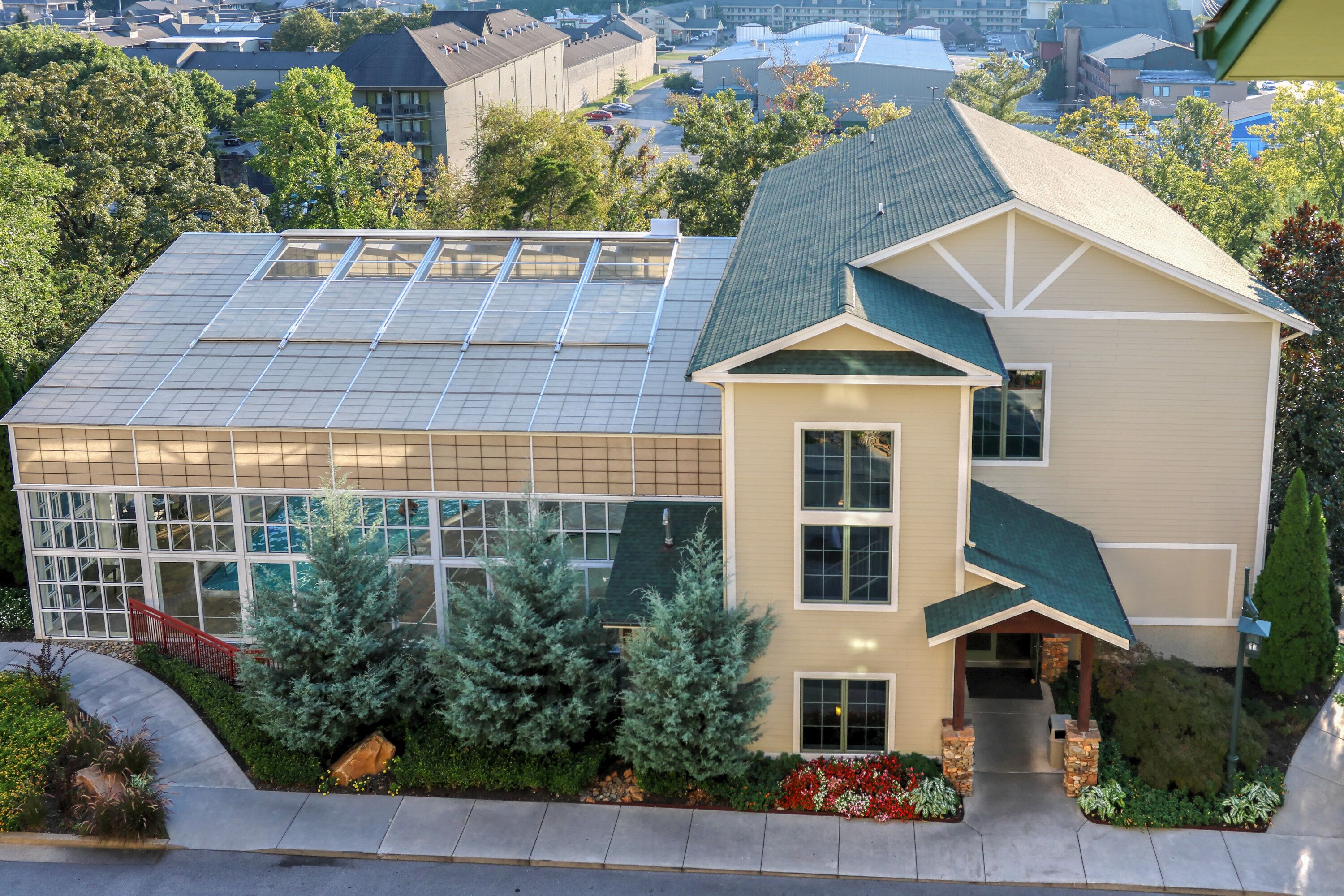 A building with a large glass facade, a green roof, and a landscaped front yard with trees and shrubs.