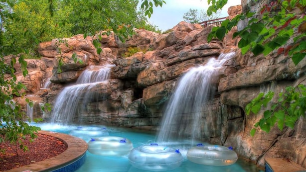 A water park with multiple water slides and inflatable tubes in a pool area surrounded by rocky terrain and greenery.