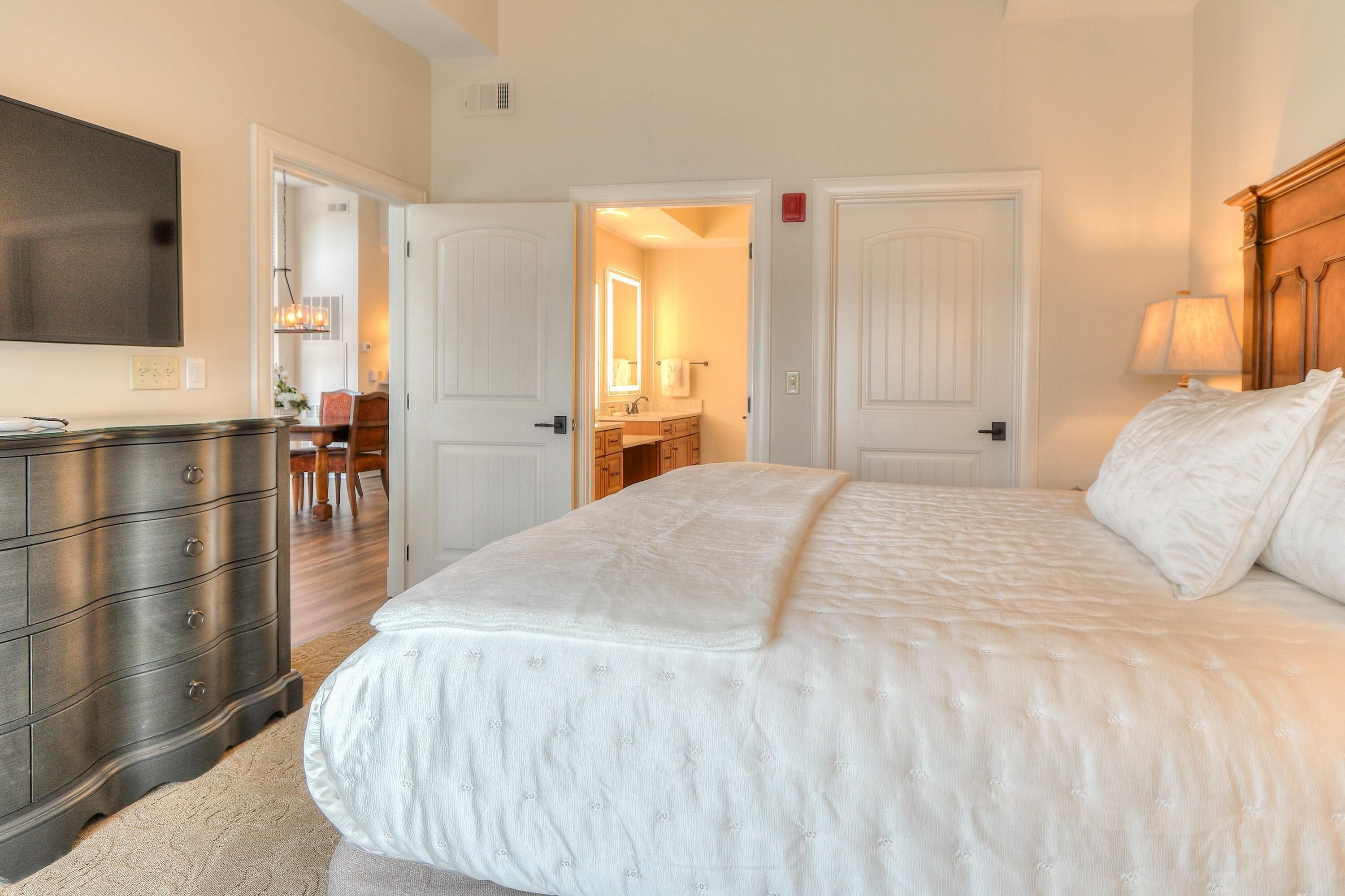 A bedroom with a large bed, a dresser, and a television on the wall.