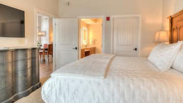 A bedroom with a large bed, a dresser, and a television on the wall.