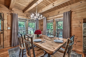 A wooden dining room with a chandelier, a table set for six, and large windows.