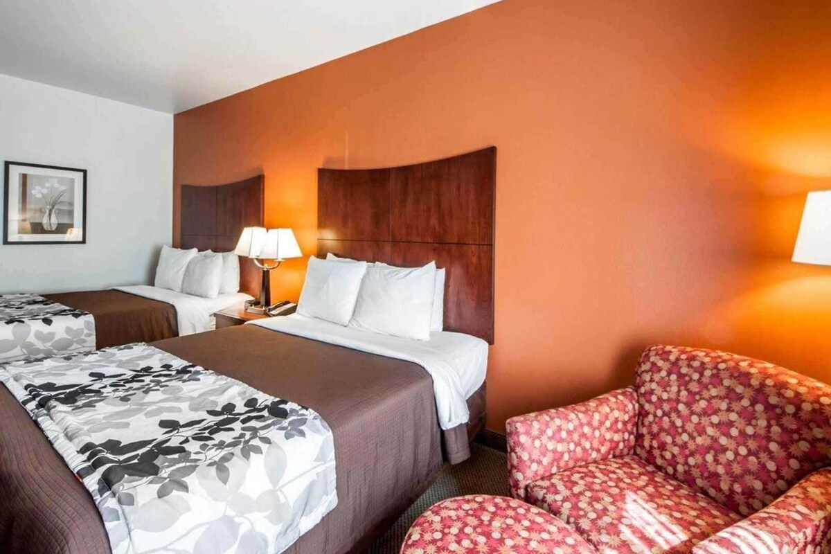 A hotel room with two beds, a sofa, a nightstand with a lamp, and a framed picture on the wall.