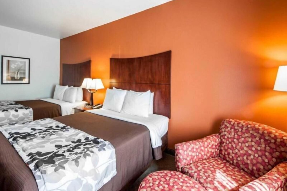 A hotel room with two beds, a sofa, a nightstand with a lamp, and a framed picture on the wall.