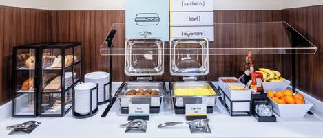 Ein reichhaltiges Buffet mit ausgewiesenen Bereichen, darunter Schweinewürste, Eier aus Freilandhaltung und eine Sandwich-Station.