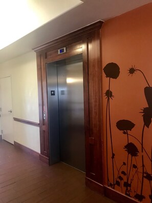 An elevator with a star sign on the door, a wooden frame, and a wall with a floral mural. - Garner Hotel Lawton Fort Sill Area by IHG (Lawton)
