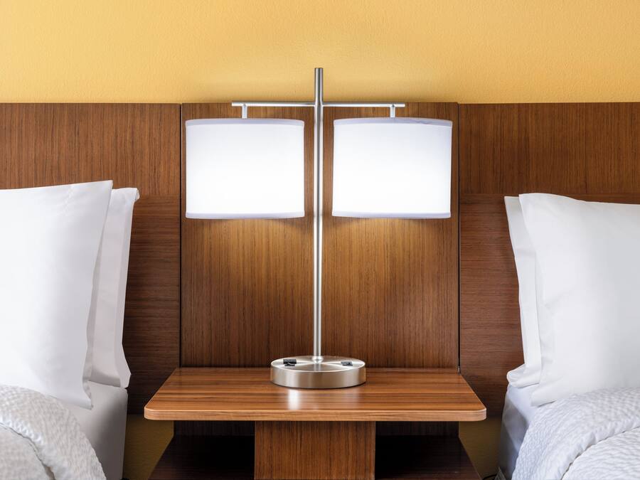 Een hotelkamer met een houten hoofdbord, twee bedden met witte lakens en een nachtkastje met een lamp.
