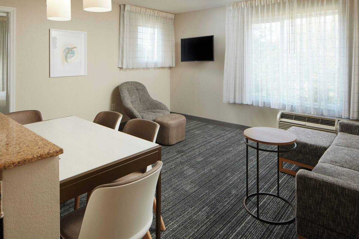 Een hotelkamer met een eettafel, twee stoelen, een bank, een ronde tafel en een flatscreen televisie aan de muur.