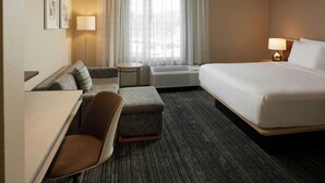 A hotel room with a bed, a desk, a chair, a small table, and a window with curtains. - TownePlace Suites by Marriott Winchester (Winchester)