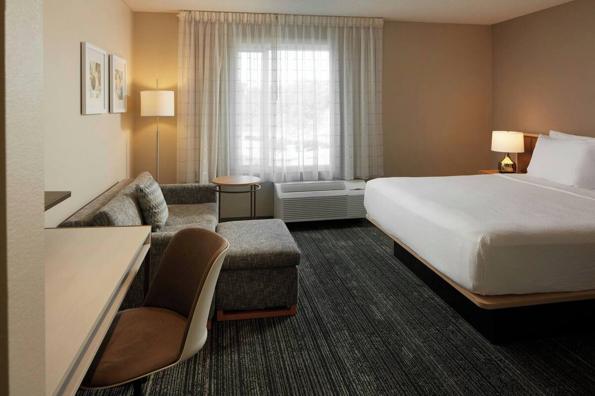 Een hotelkamer met een bed, een bureau, een stoel, een klein tafeltje en een raam met gordijnen.