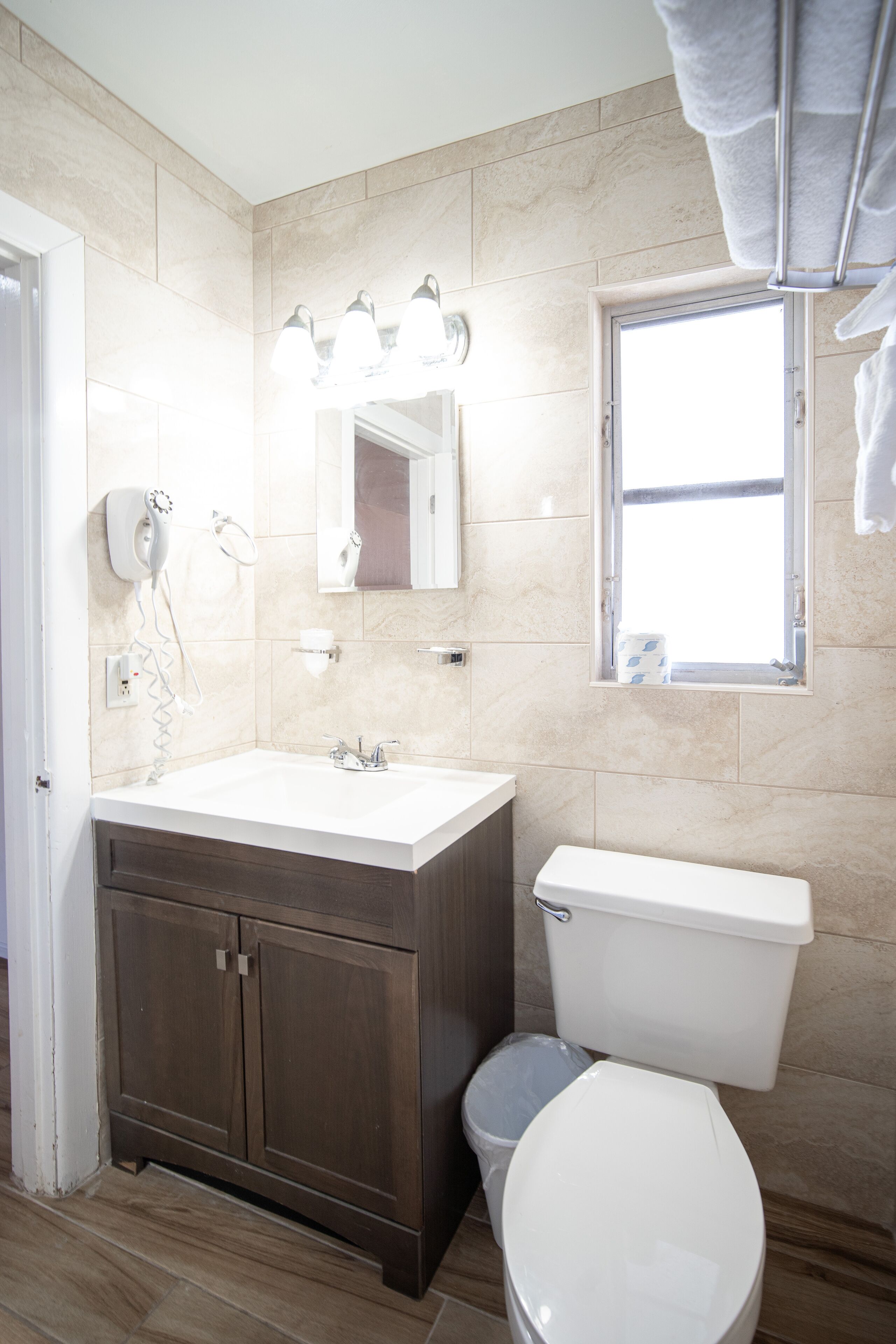 A modern bathroom with a white sink, dark wooden cabinets, a white toilet, and a window with a towel rack.