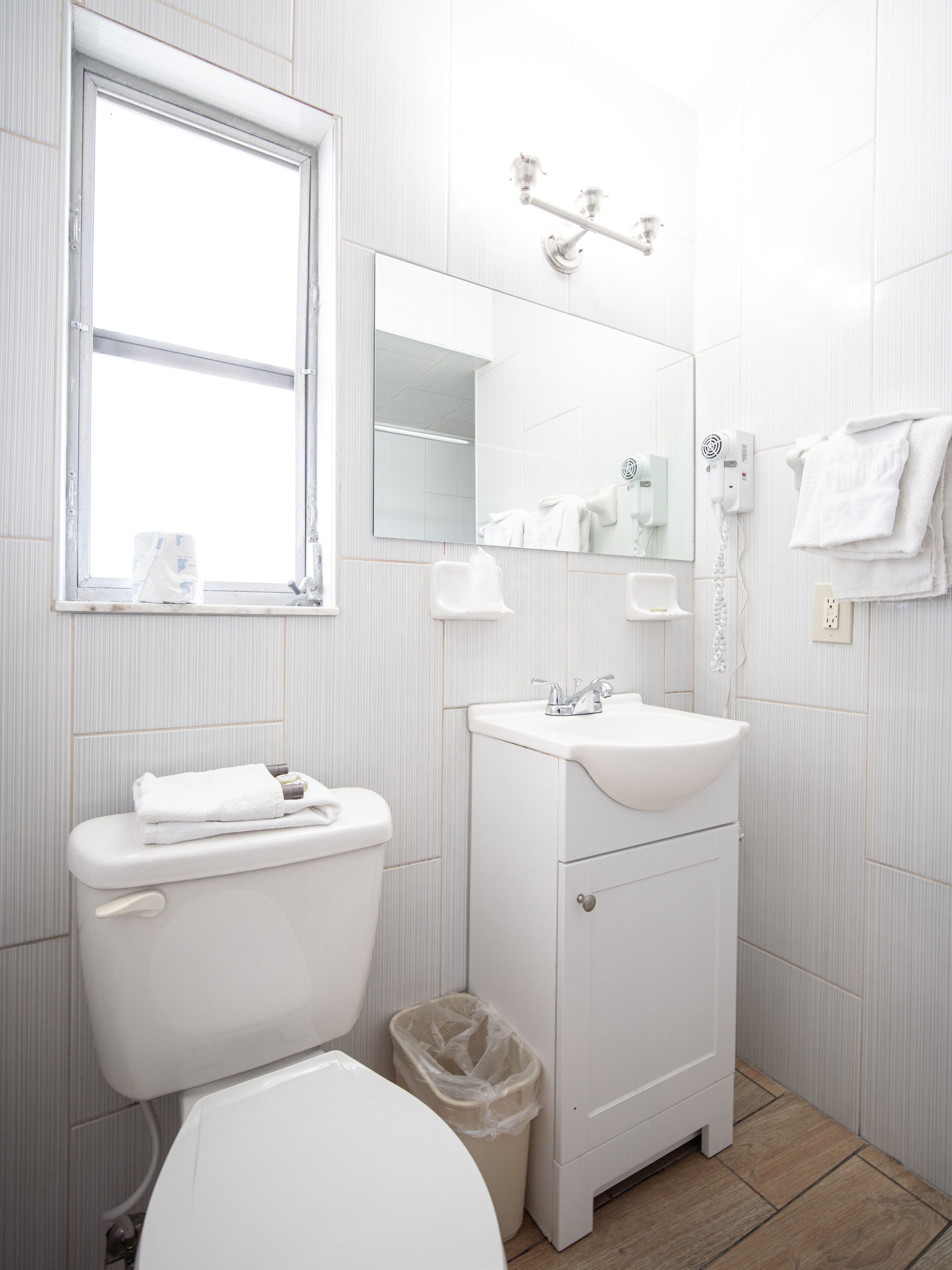 A modern bathroom with a toilet, sink, mirror, and window.
