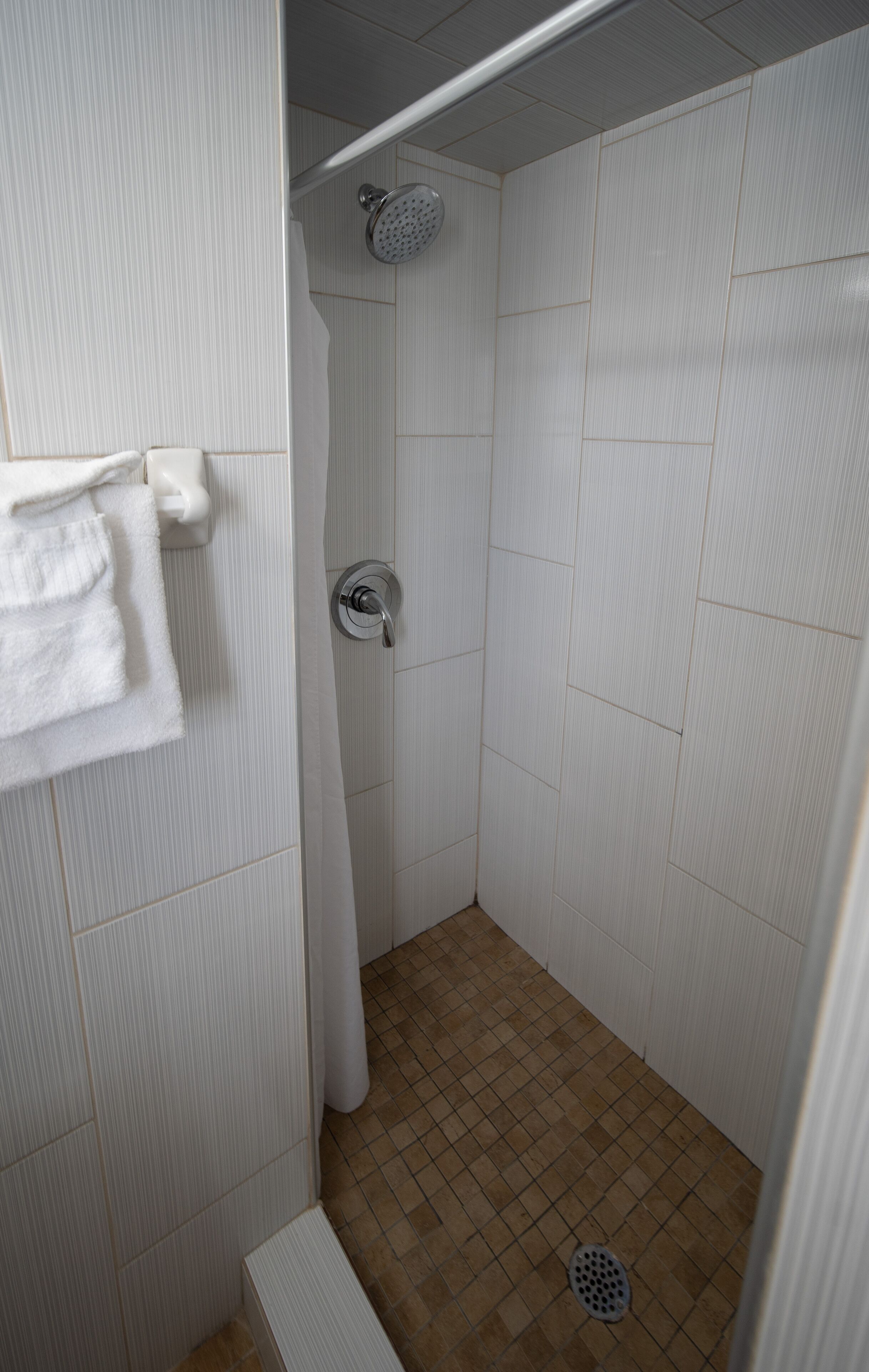 Un baño pequeño con azulejos, un cabezal de ducha, un perchero y un desagüe.