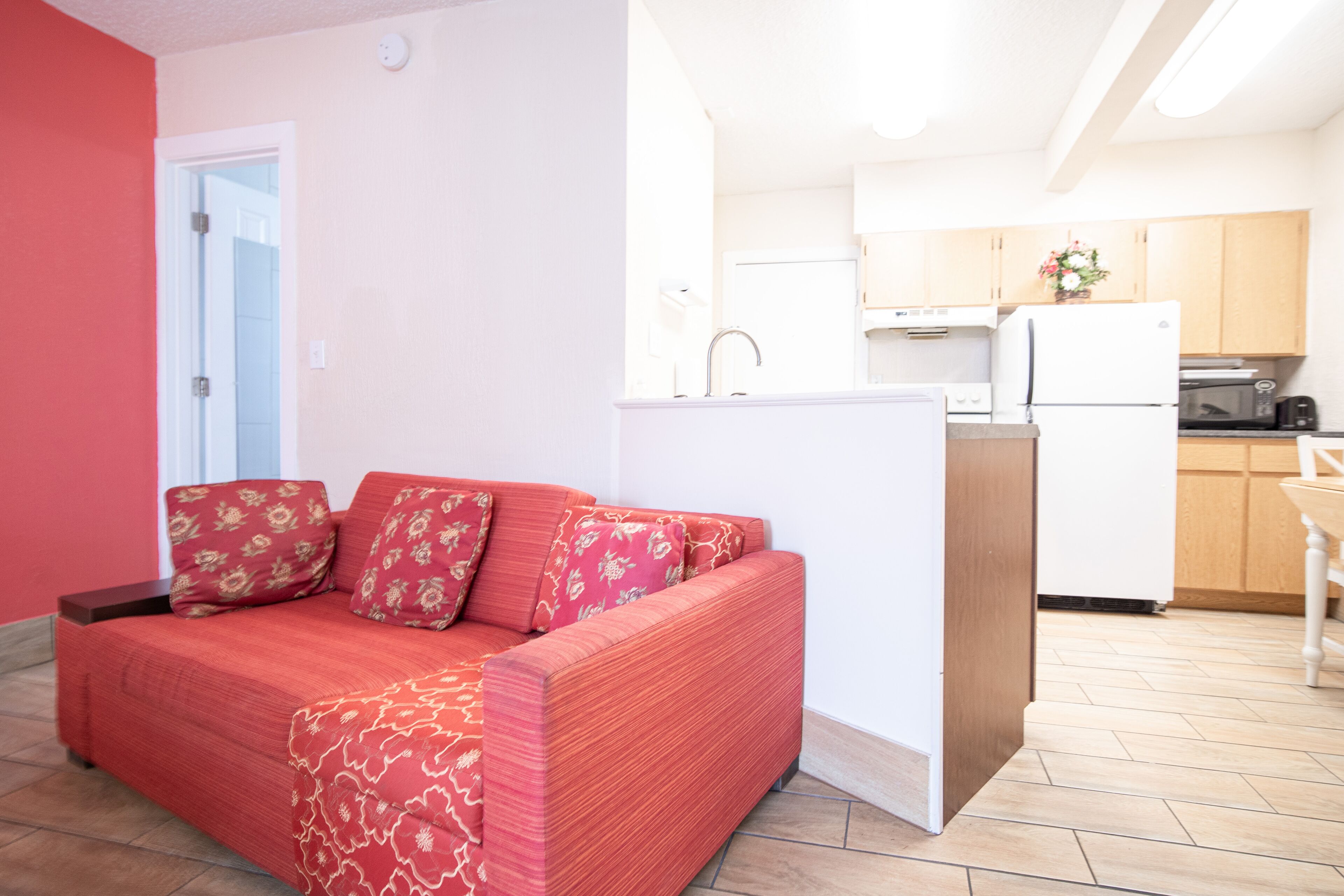 A compact living space with a red sofa, a small kitchen area, and a door leading to another room.