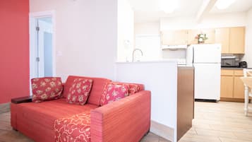 Un espacio habitable compacto con un sofá rojo, una pequeña cocina y una puerta que da a otra habitación.