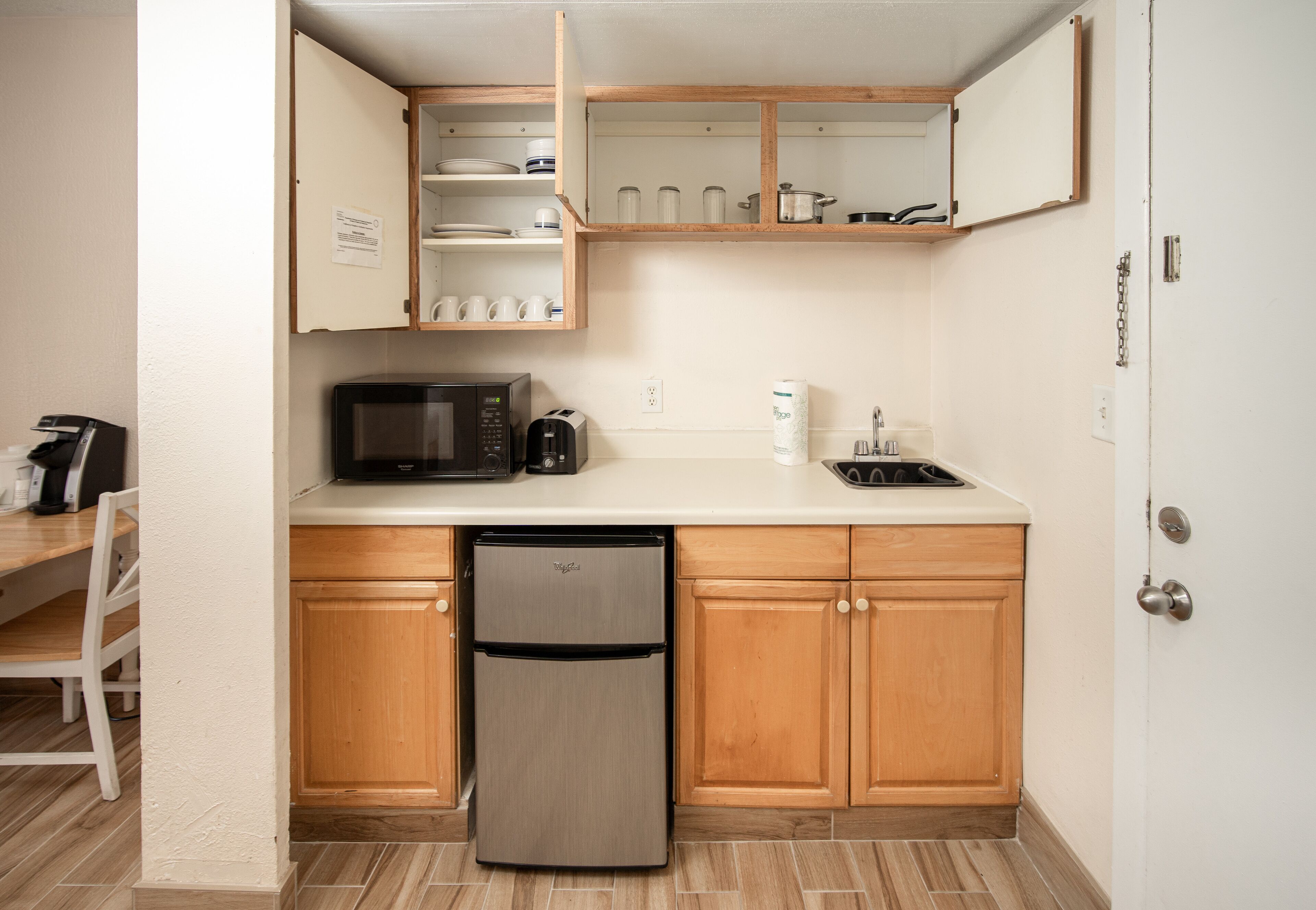 Una cocina compacta con armarios de madera, microondas integrado, refrigerador y pileta.