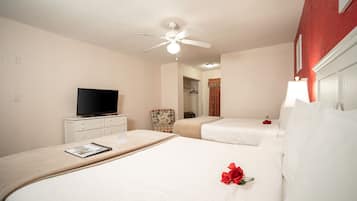 A hotel room with two beds, a ceiling fan, a television on a dresser, and a red rose on one bed.