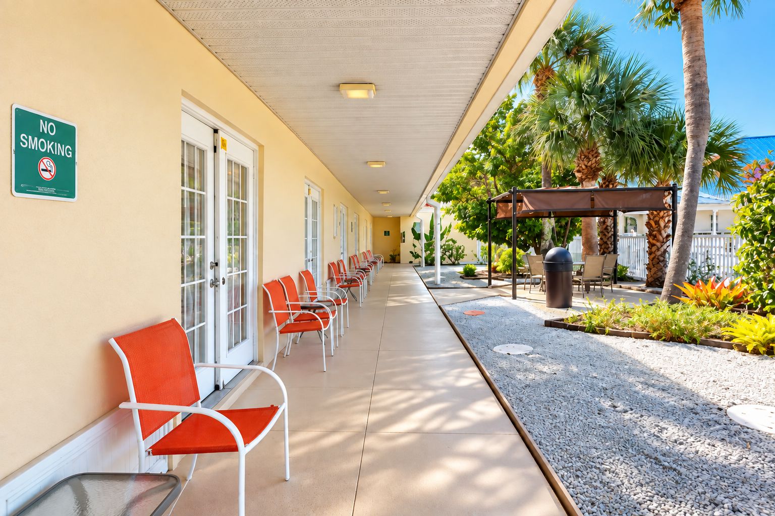 A hotel corridor with a 'NO SMOKING' sign, outdoor seating, and palm trees.