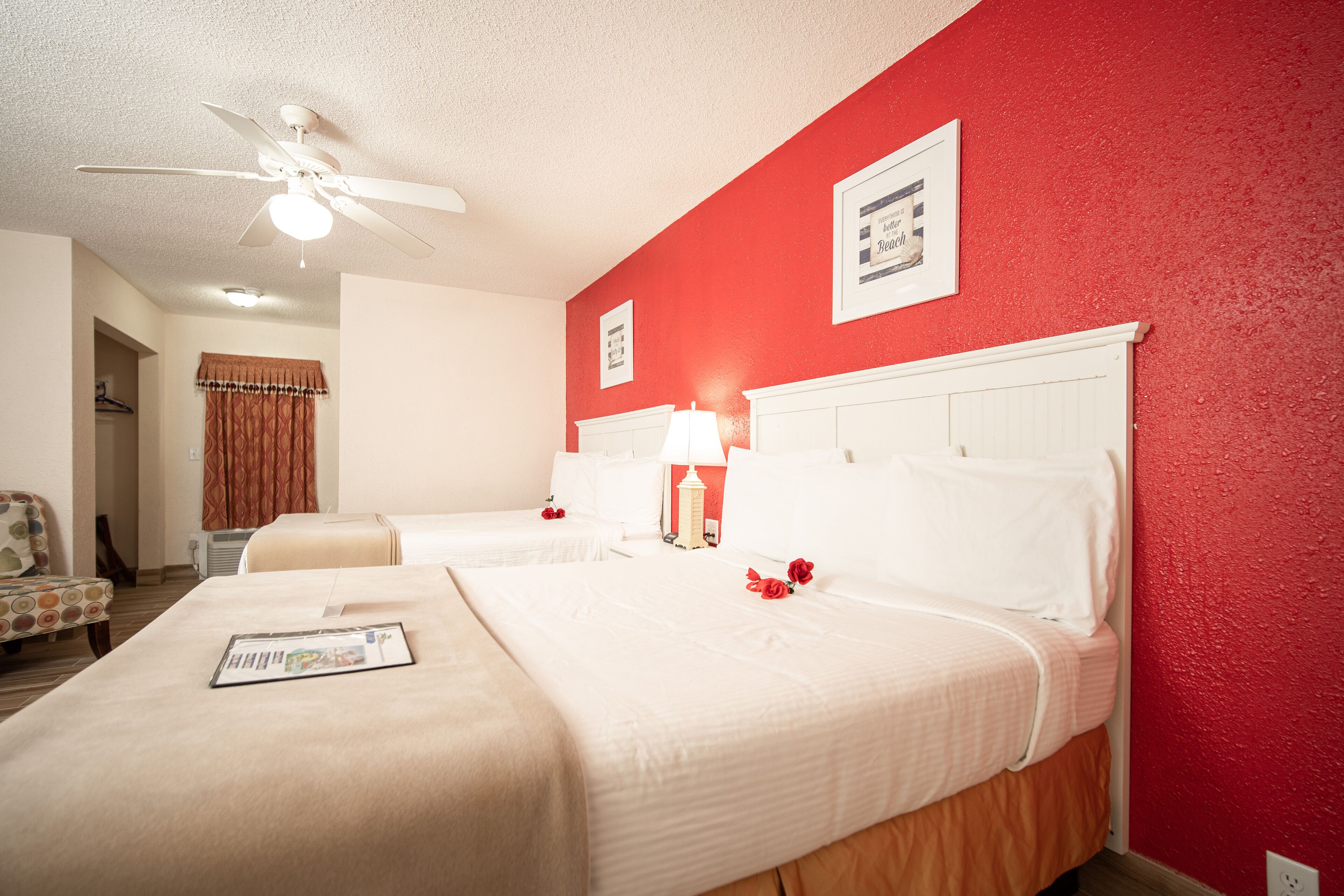 Habitación de hotel con dos camas, ventilador de techo, pared de acento roja y un cuadro enmarcado en la pared.