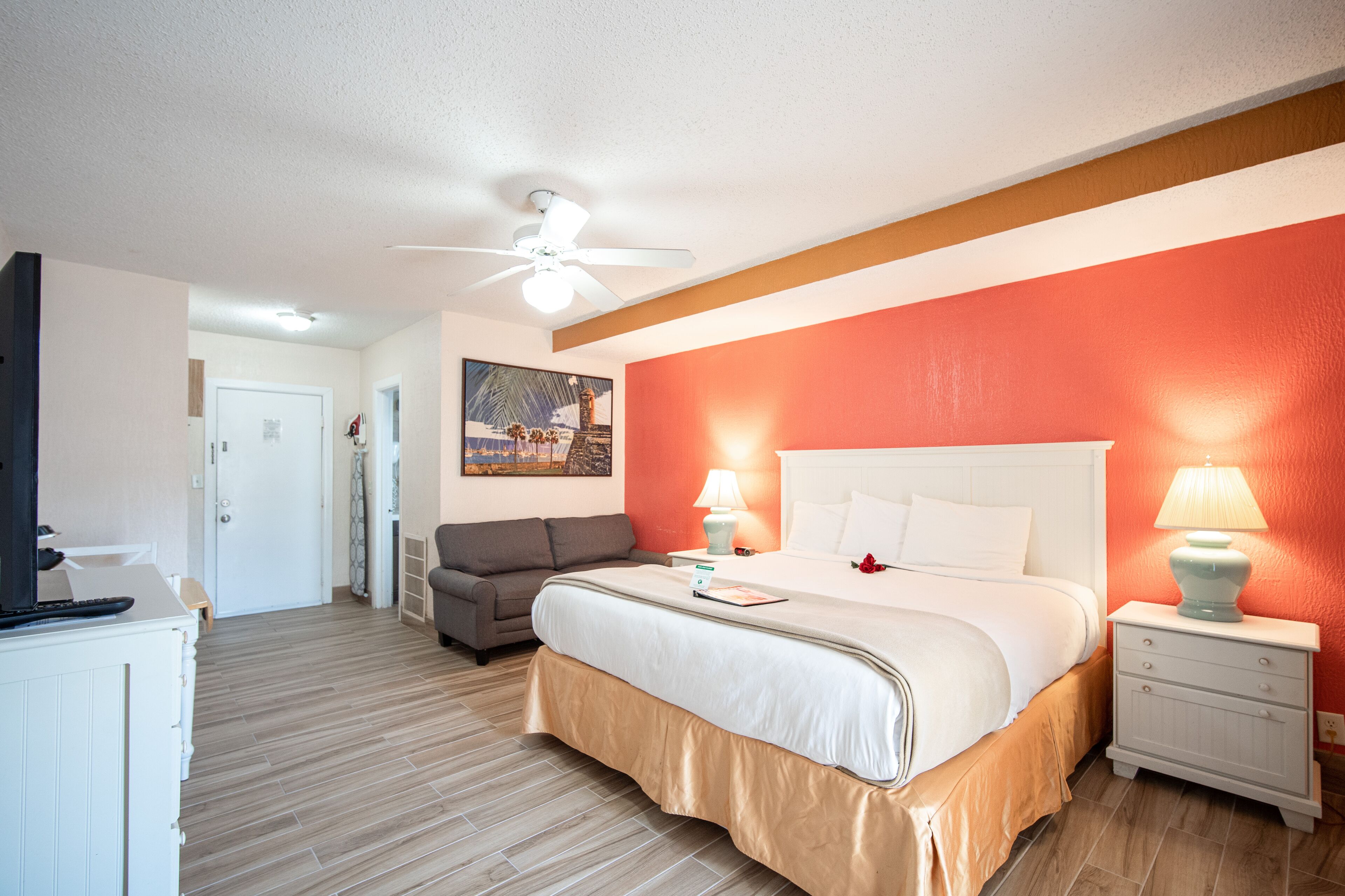 A bedroom with a bed, bedside tables, a ceiling fan, a desk, and a chair.