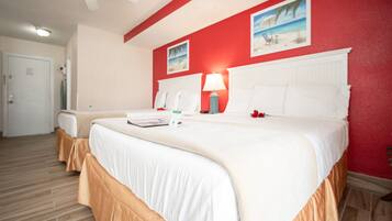 A hotel room with two beds, a red accent wall, and a beach-themed picture.