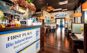 Interior de un restaurante con barra, cabinas de comedor y mostrador con un cartel que indica que es el 'Primer Lugar' para el desayuno.