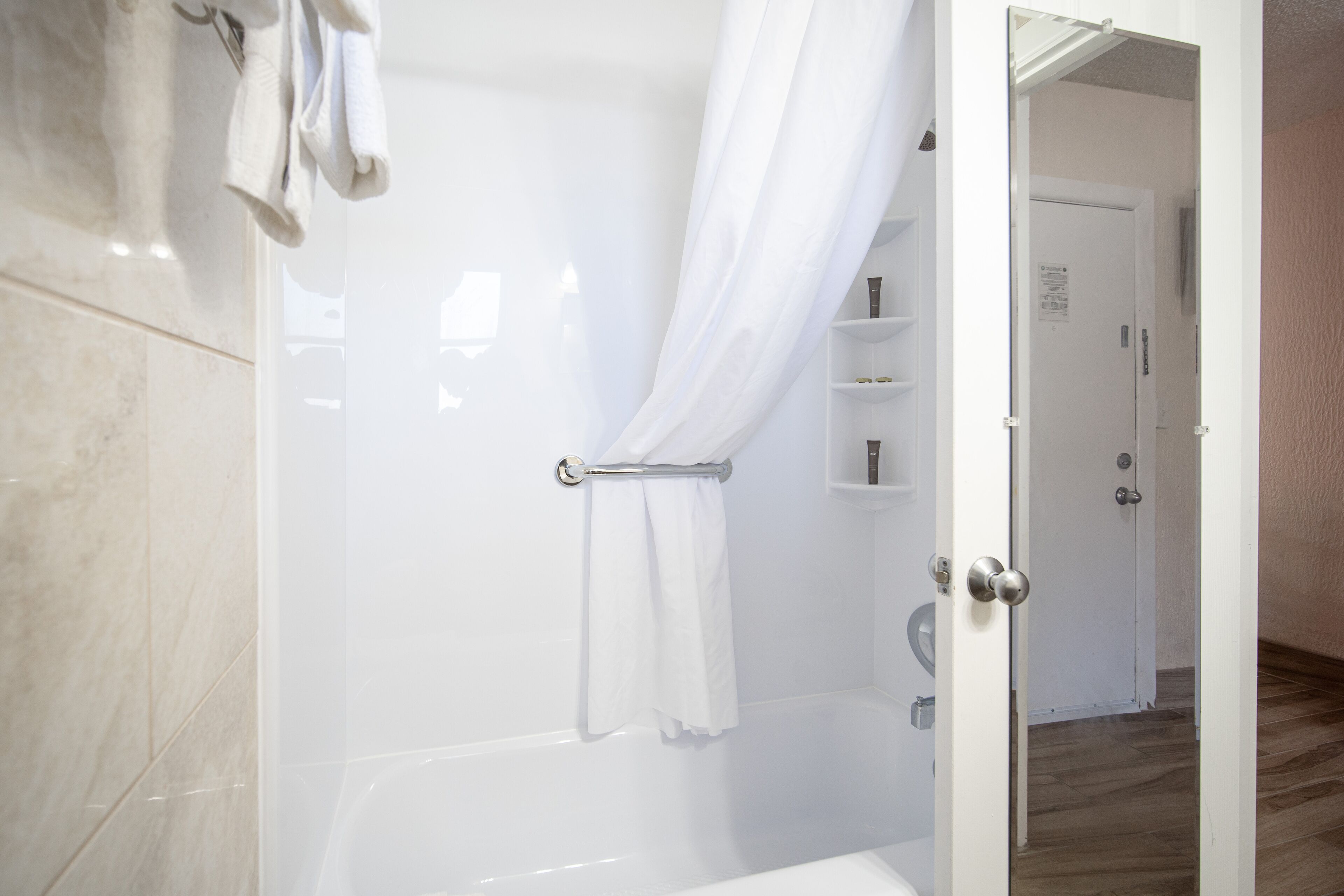Une salle de bain moderne avec une douche à l’italienne en verre, une baignoire blanche et une porte donnant sur une autre pièce.