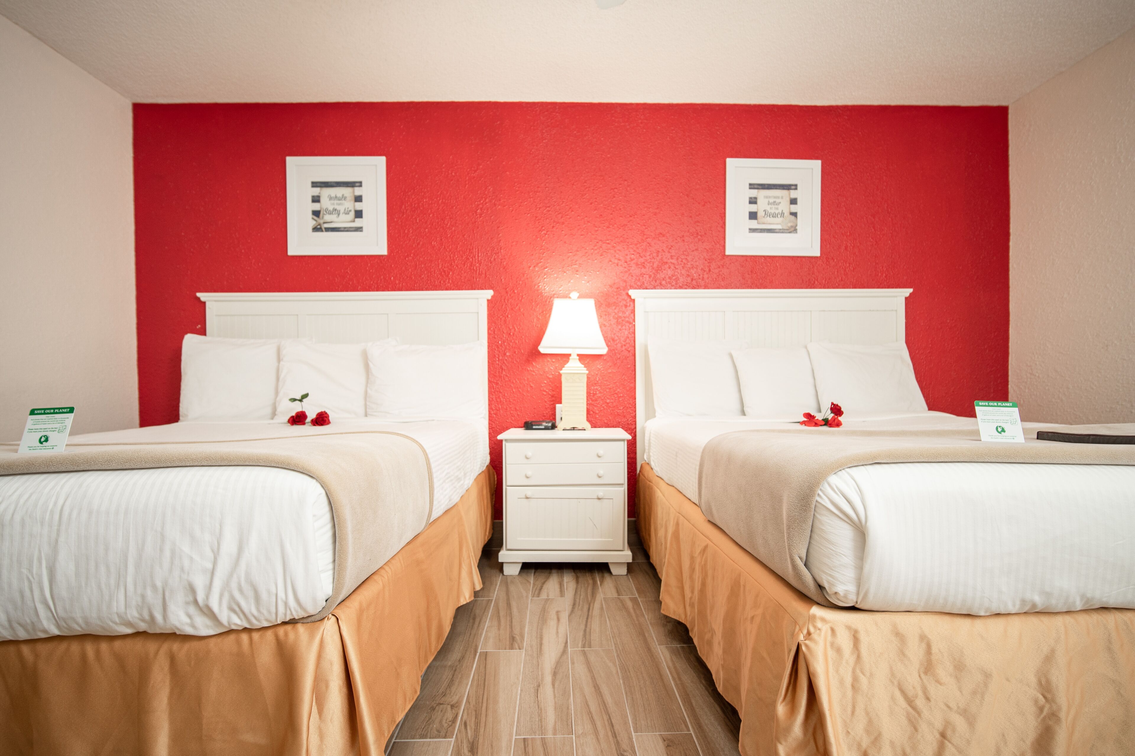 A hotel room with two beds, a nightstand with a lamp, and red walls.