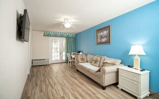 Una sala de estar con un sofá color crema, una mesita de noche blanca, un ventilador de techo y una pared azul.