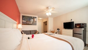 Een hotelkamer met een bed, een plafondventilator, een televisie en een koelkast.