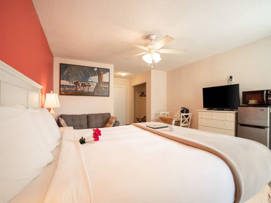 A hotel room with a bed, a ceiling fan, a TV, and a refrigerator.