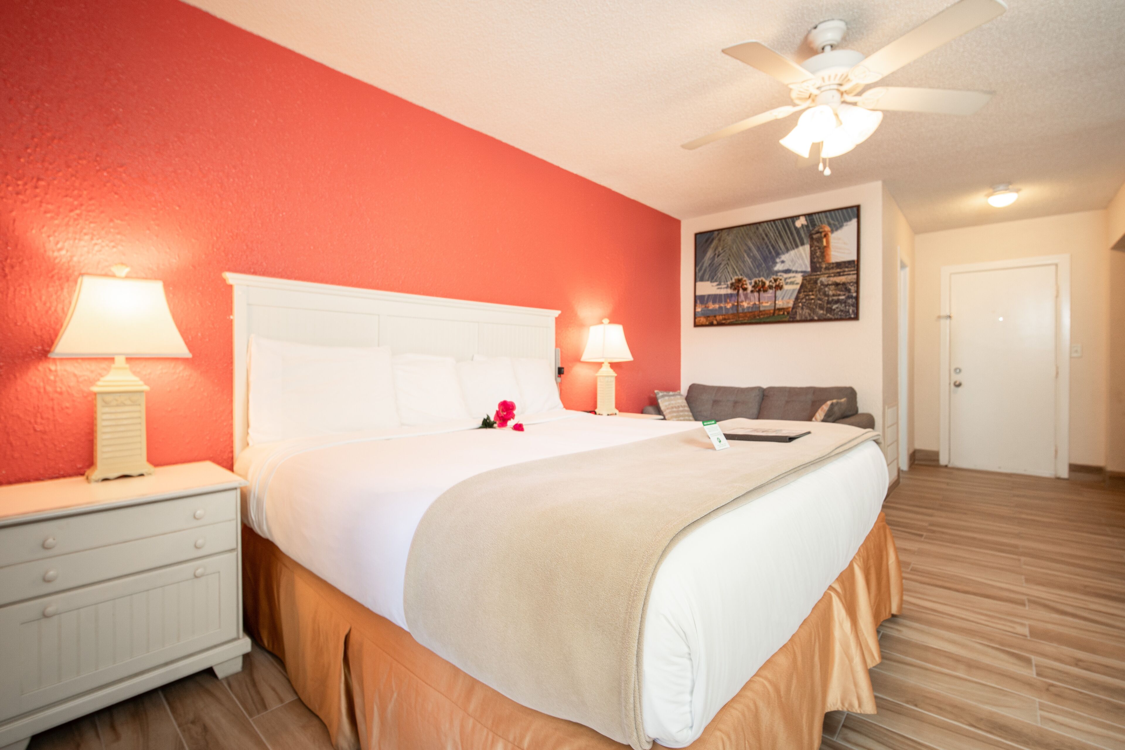 Habitación de hotel con cama, mesitas de noche, ventilador de techo y un cuadro en la pared.