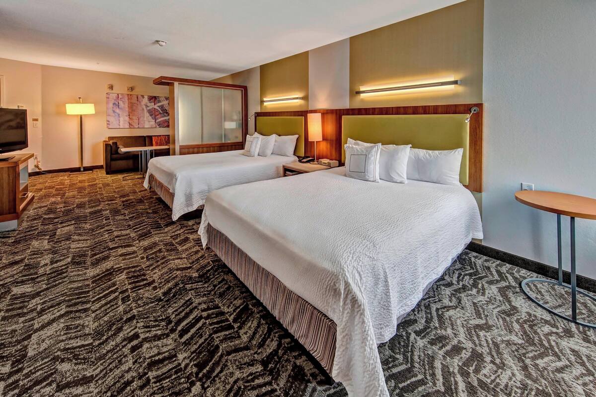 A hotel room with two beds, a sofa, a desk, and a TV.