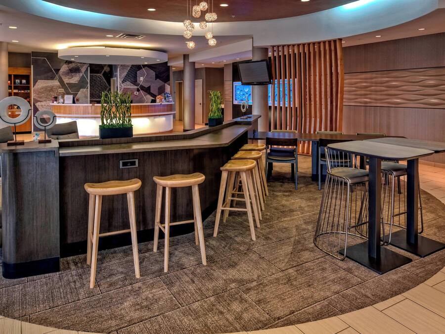 Una zona de bar moderna con una barra curva, taburetes de madera y un espacio de estar con mesa y sillas.