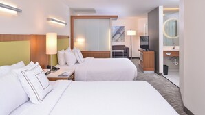 Habitación de hotel con dos camas, un escritorio con silla, televisor y baño con espejo.