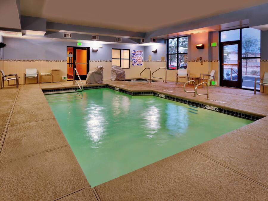 An indoor swimming pool with clear water, tiled walls, and a tiled floor. There are chairs and a covered area for changing.