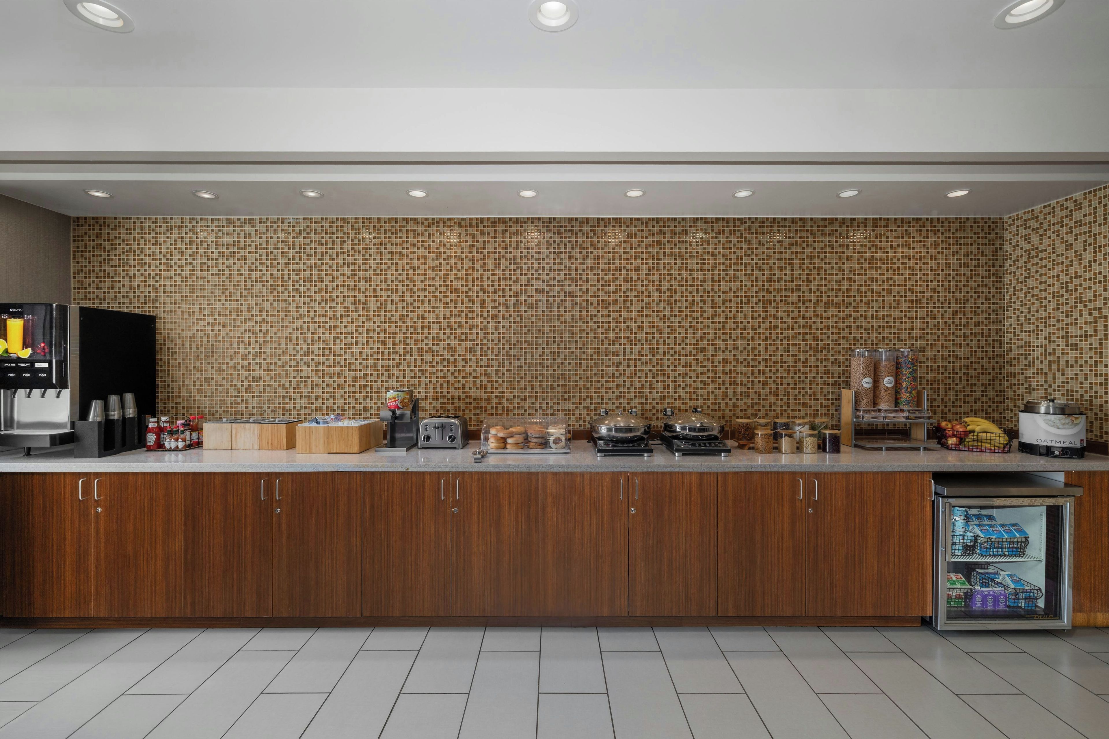 A modern kitchen with a tiled backsplash, a coffee station, and a refrigerated display.