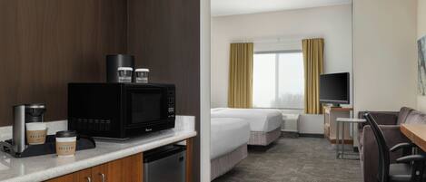 A hotel room with a kitchenette, a bed, a desk, a chair, a television, and a window with curtains.